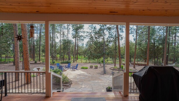 A wooden deck with a stone patio, outdoor seating, and a view of a forested area. - AMAZING 4300 SQ FEET RETREAT ON  4.5 ACRES WITH AC!! SLEEPS 16 PETS WELCOME! (Pinetop-Lakeside)