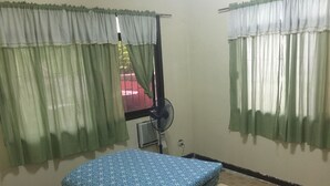 A room with a bed, a standing fan, and curtains. - Gated community (Davao city)