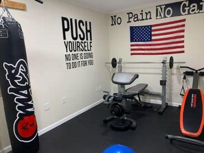 Un gimnasio con arte motivacional en la pared, un saco de boxeo y equipo de levantamiento de pesas.