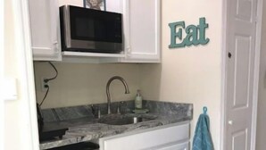 A compact kitchen with white cabinets, a stainless steel refrigerator, a microwave, and a sink. A towel hangs on the door handle. - Private Suite · Patio · BBQ · GYM · Beach: 5 Miles (Largo)
