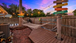 Una hamaca entre dos palmeras, una terraza de madera y carteles indicando diferentes destinos.