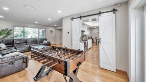 Amplia sala de estar con mesa de fútbol, sofá de cuero y cocina al fondo.
