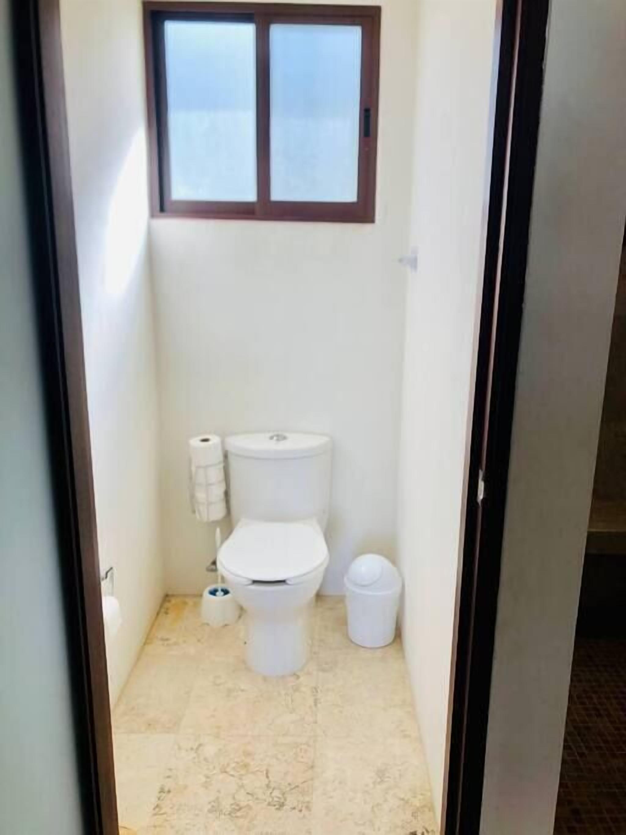 A small, narrow bathroom with a toilet, a small trash bin, and a toilet paper holder.