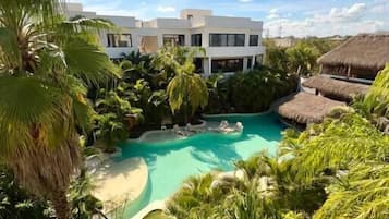 Ein Resort mit Pool, umgeben von tropischer Vegetation, mit einem modernen Gebäude im Hintergrund.