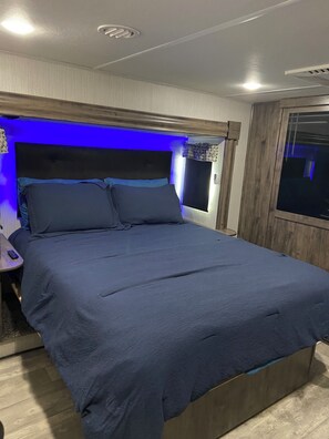 A bed with a headboard, a bedside table with a lamp, and a window with curtains.