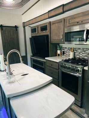 A compact kitchen with a sink, stove, microwave, and cabinets. - Waterfront Glamping (Lufkin)