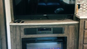 Een flatscreen televisie bevestigd aan een houten kast, daaronder een open haard, en een keuken aan de rechterkant.