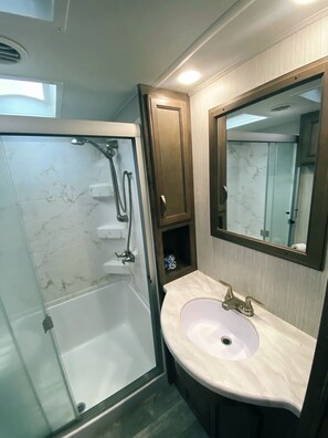 A bathroom with a glass-enclosed shower, a sink with a marble countertop, and a mirror above the sink. - Waterfront Glamping (Lufkin)
