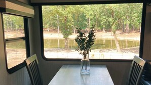 Een eethoek met een tafel en stoelen, een vaas met een plant, en uitzicht op een bebost gebied door een raam.