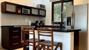Una cuina moderna amb una illa central, armaris foscos, un frigorífic d'acer inoxidable i una finestra que deixa entrar llum natural.