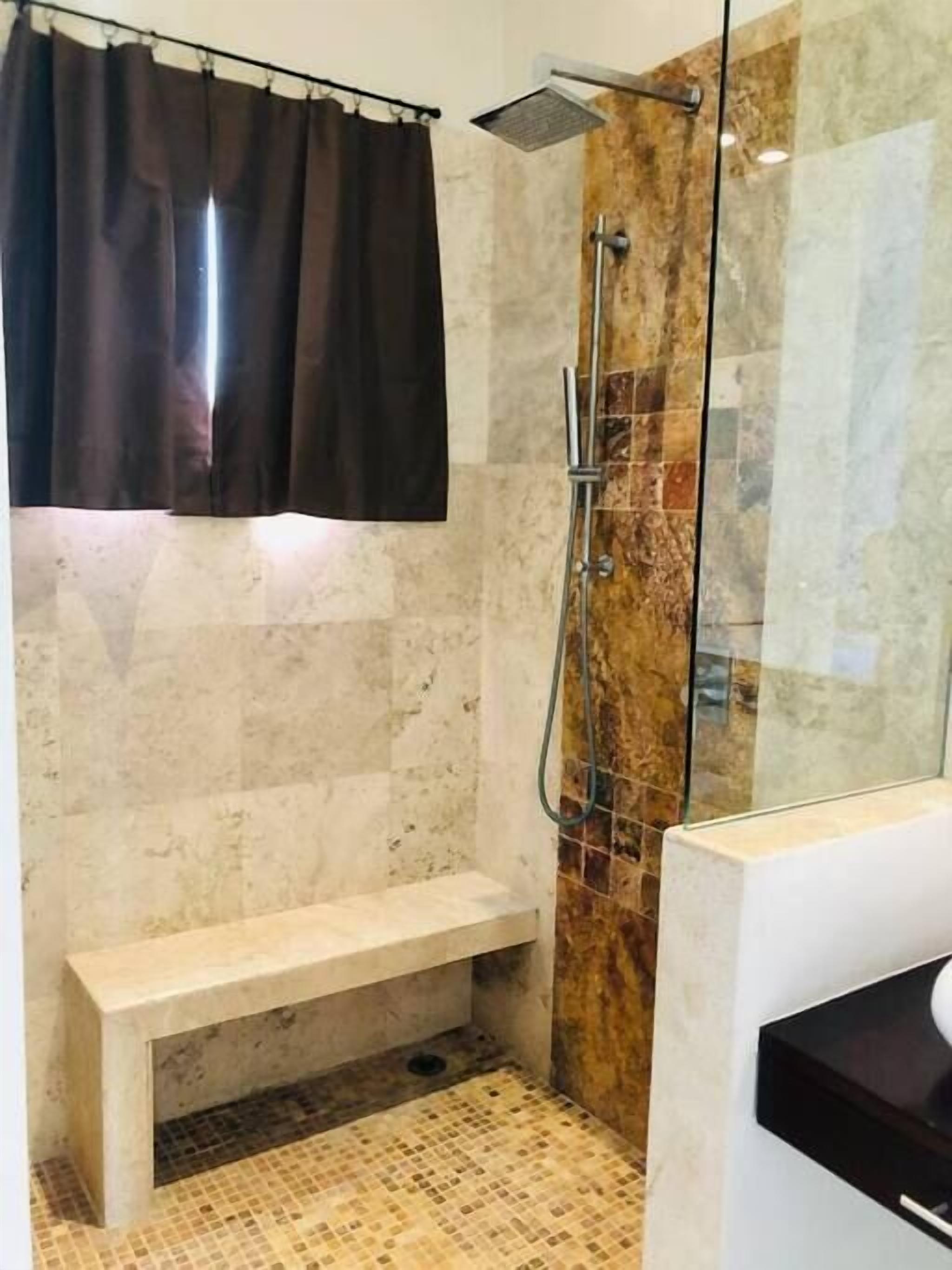 Un baño con ducha, un banco y piso de baldosas.