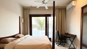 Habitació d'hotel amb un llit amb cortines i pilars, un escriptori i un ventilador de sostre.