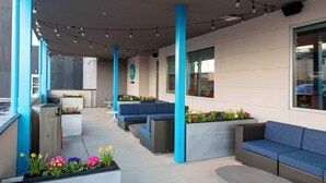 An outdoor seating area with blue sofas and planters with flowers. - Tru By Hilton Manteca, Ca (Manteca)