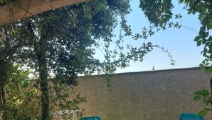 Ein Gartenbereich mit zwei blauen Liegestühlen unter einer Pergola, umgeben von Grünpflanzen und einer Steinmauer.