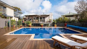 Relax by the clear pool surrounded by a deck with lounge chairs and potted plants.