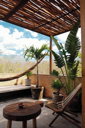 A covered outdoor seating area with a hammock, wooden chairs, and potted plants. - Galopina (Seyé)