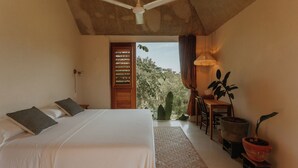 A bedroom with a bed, a ceiling fan, a desk with a chair, and a potted plant. - Galopina (Seyé)