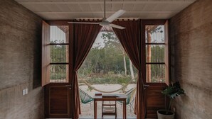 A room with a hammock, a table, and a chair, with a view of a natural landscape through open wooden doors. - Galopina (Seyé)