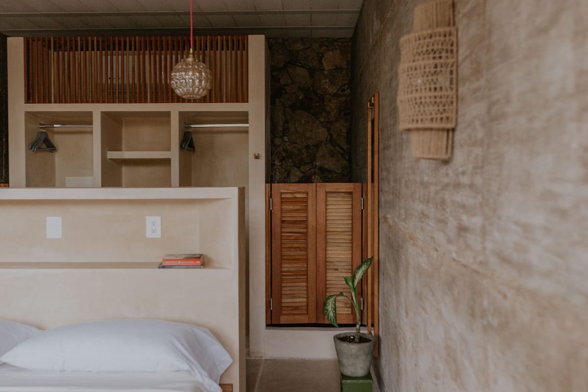 Un dormitorio con una cama, un armario de madera, una planta en maceta y una lámpara colgante.