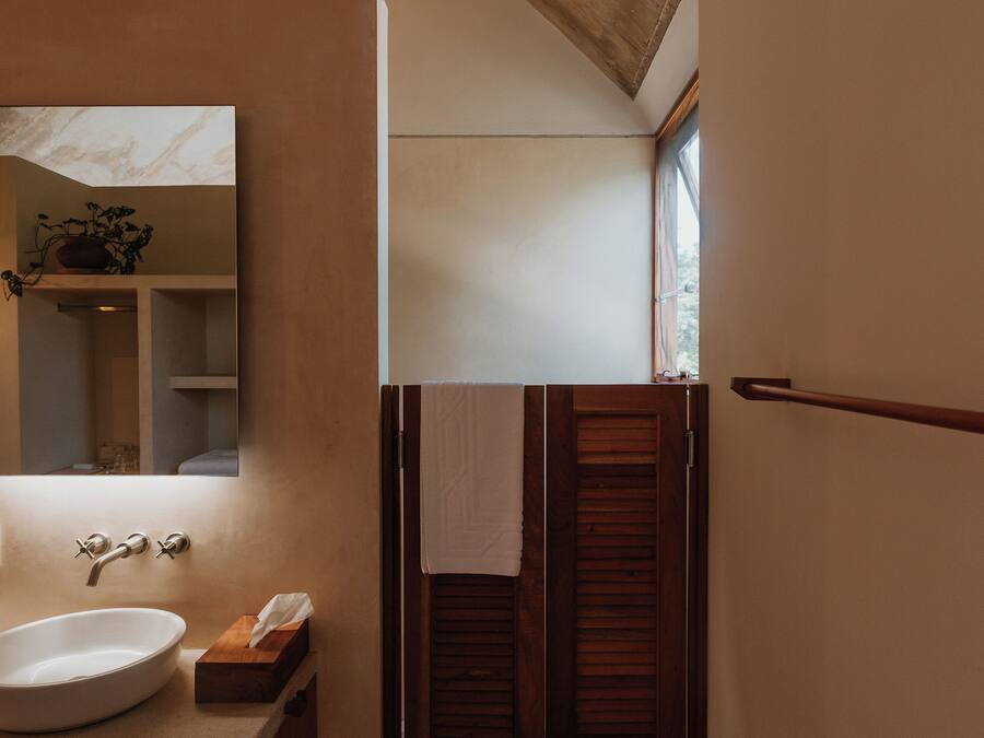 Een badkamer met een houten plafond, een grote spiegel, een wastafel en een raam met houten luiken.