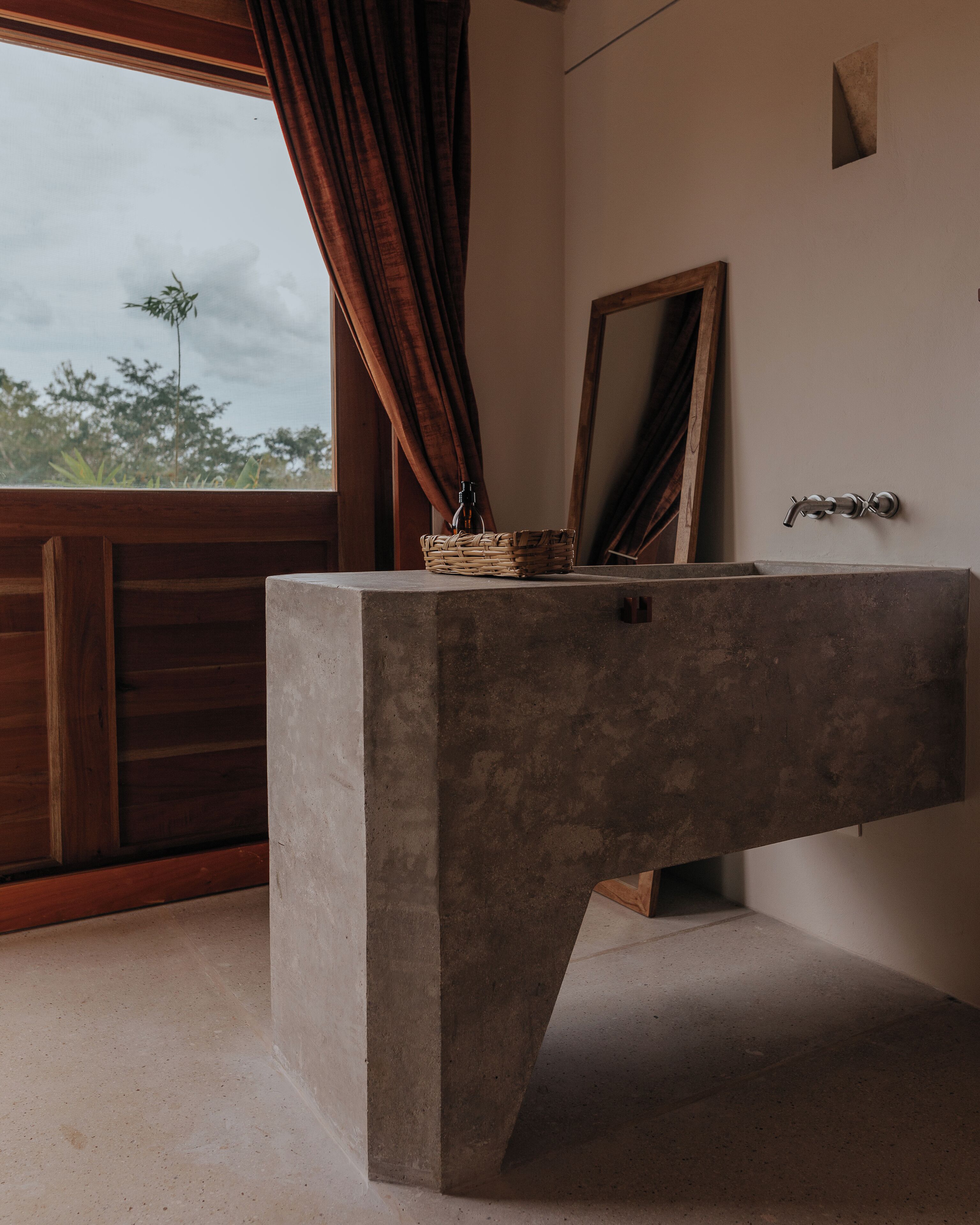 Un bagno con un lavandino in cemento, una porta in legno e una finestra con tende.