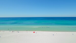 A wide sandy beach with clear turquoise water and a few people in the distance.