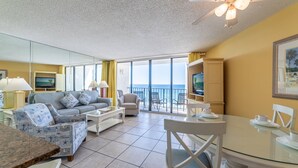 A spacious living room with a large window overlooking the sea, a ceiling fan, and a dining area with a glass table.