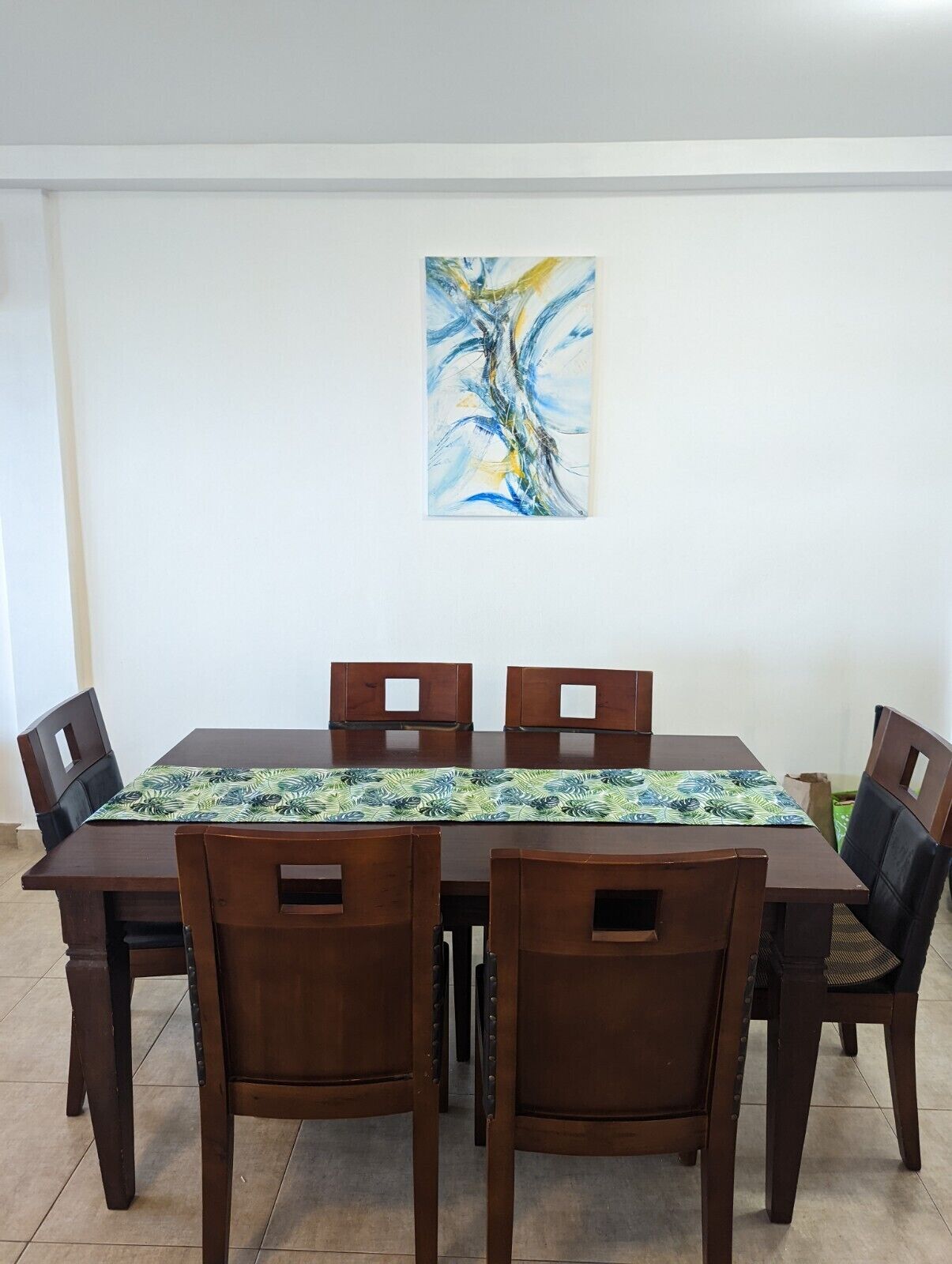 A dining area with a rectangular table, four wooden chairs, and a colorful table runner.