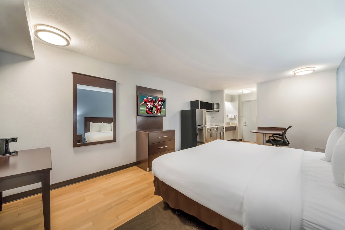 Une chambre d’hôtel avec un grand lit, un bureau, un miroir, une télévision, une armoire et une kitchenette.