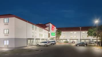 Un hotel con varios pisos, un estacionamiento con varios autos y un llamativo letrero de Red Roof Inn.