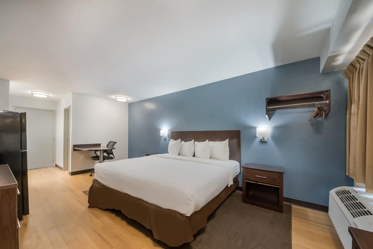 Une chambre d’hôtel avec un grand lit, un bureau, une chaise, une armoire et un radiateur fixé au mur.