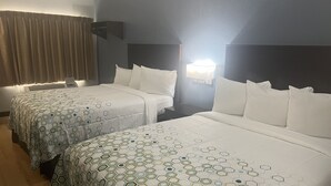 A hotel room with two beds, each with a patterned bedspread, a nightstand, a wall-mounted lamp, and a window with curtains. - HomeTowne Studios by Red Roof San Antonio - Seaworld/Northwest (San Antonio)