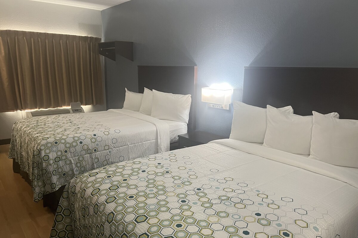 Hotelkamer met twee bedden, elk met een beddekleed met dessin, een nachtkastje, een wandlamp en een raam met gordijnen.