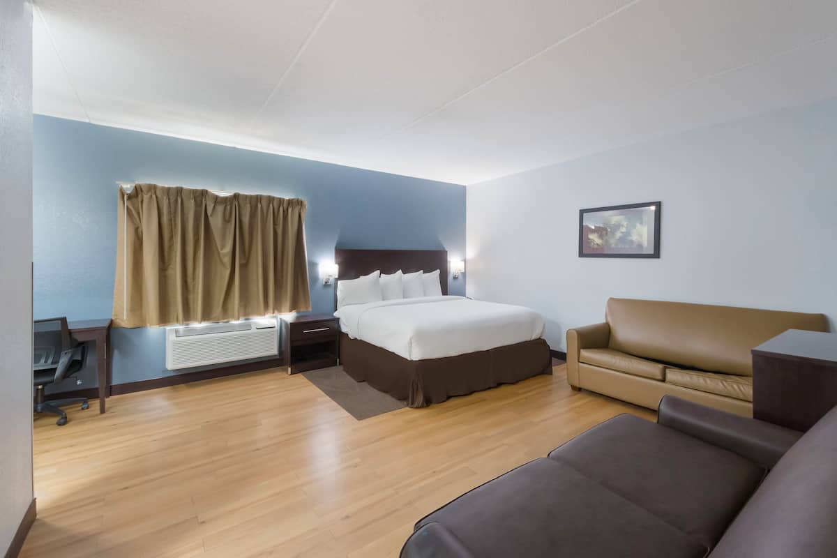 Une chambre d’hôtel avec un lit, un canapé, un bureau et une fenêtre avec des rideaux.