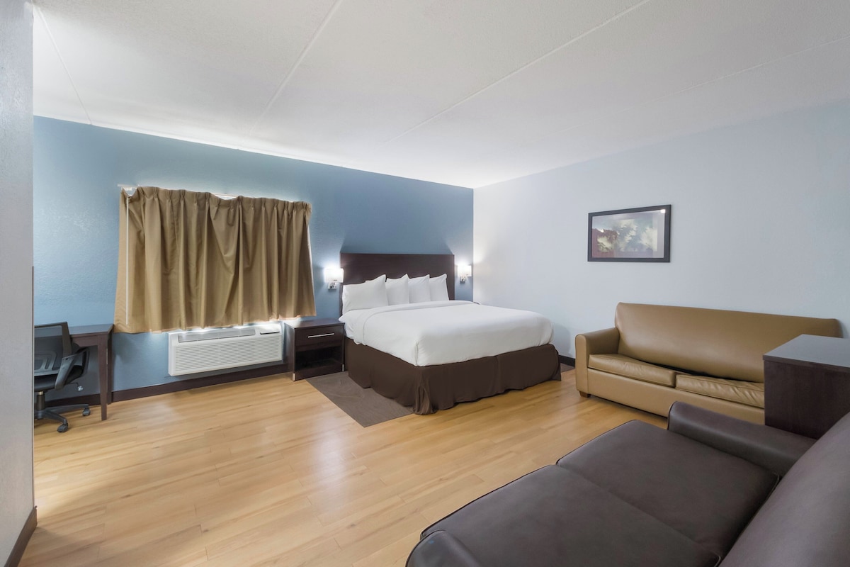 Una habitación de hotel con cama, sofá, escritorio y ventana con cortinas.