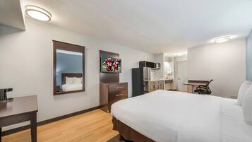 A hotel room with a bed, a desk, a mirror, a television, and a kitchenette.