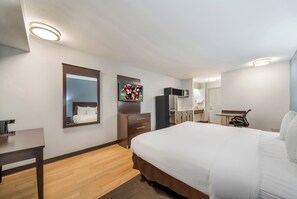 Une chambre d’hôtel équipée d’un lit, d’un bureau, d’un miroir, d’une télévision et d’une kitchenette.