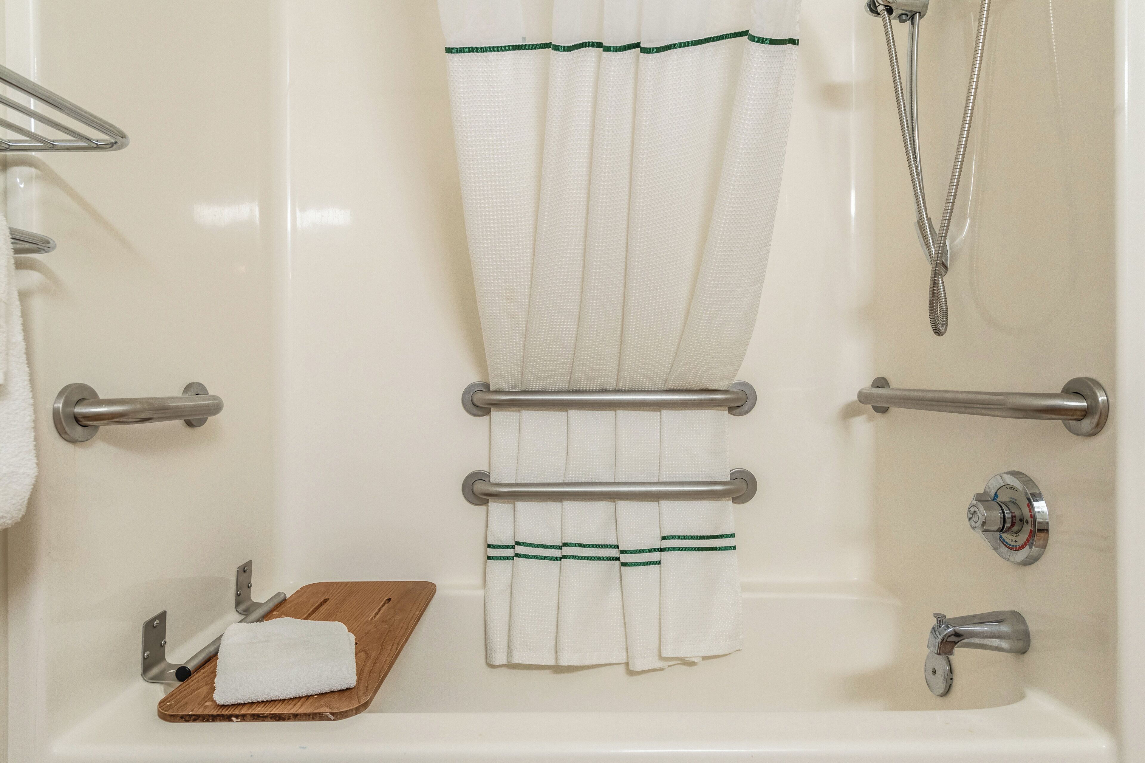 A bathroom with a bathtub, a shower, a towel rack, and a wooden tray with a towel.