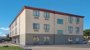 Un edificio de varios pisos con techo plano, grandes ventanales y un estacionamiento frente a él.
