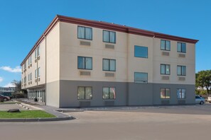 Un edificio de varios pisos con techo plano, grandes ventanales y un estacionamiento frente a él.