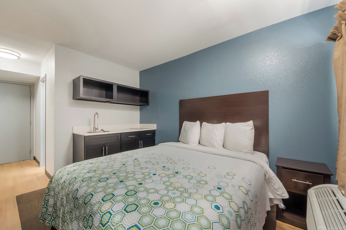 Habitación de hotel con una cama grande, una mesita de noche, una repisa empotrada y un ventanal con cortinas.