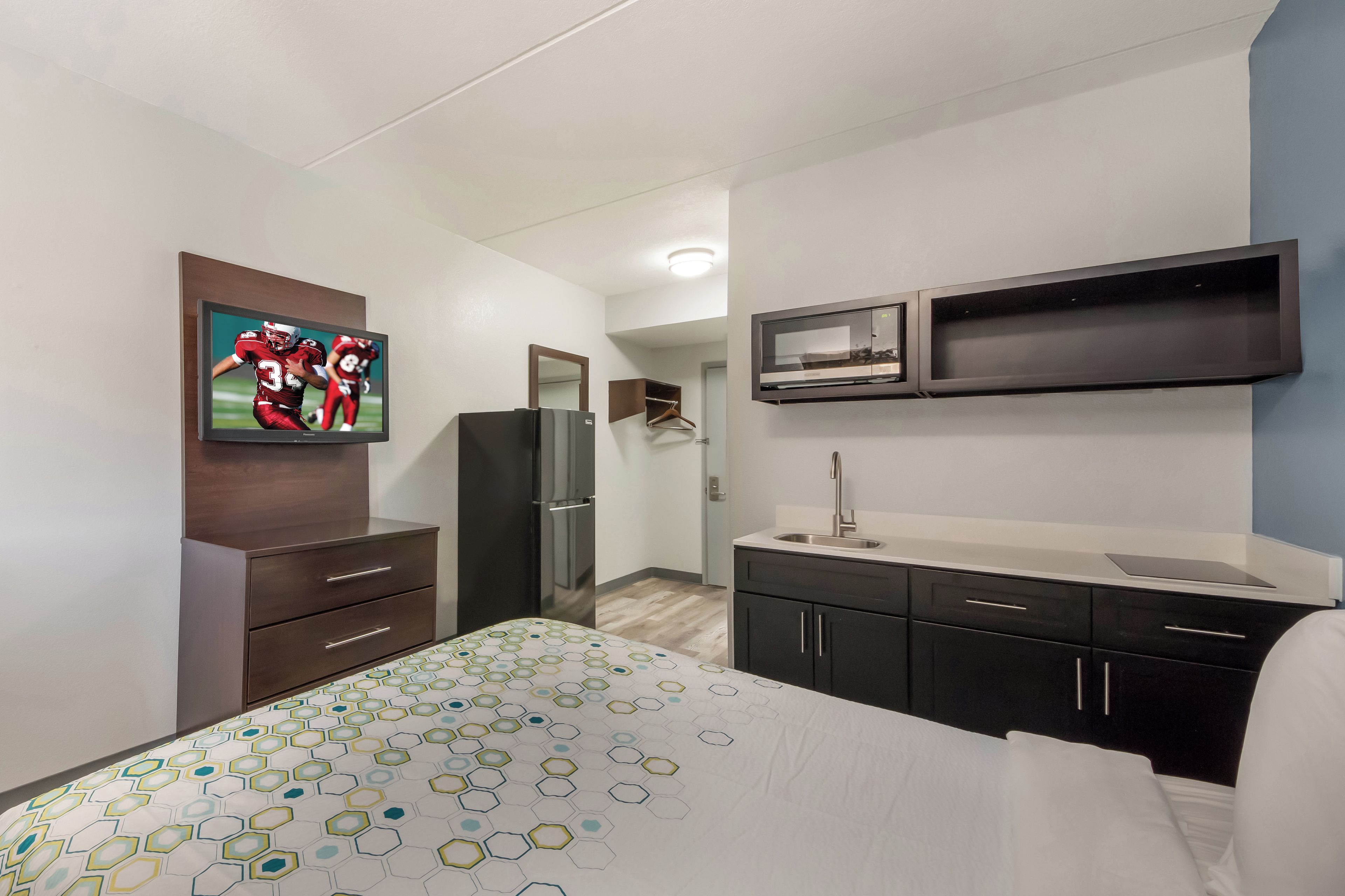 A hotel room with a bed, a TV, a refrigerator, a microwave, a sink, and a wardrobe.