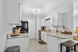 Eine kompakte Küche mit weißen Schränken, einer Granit Arbeitsplatte und einem Edelstahl-Kühlschrank.