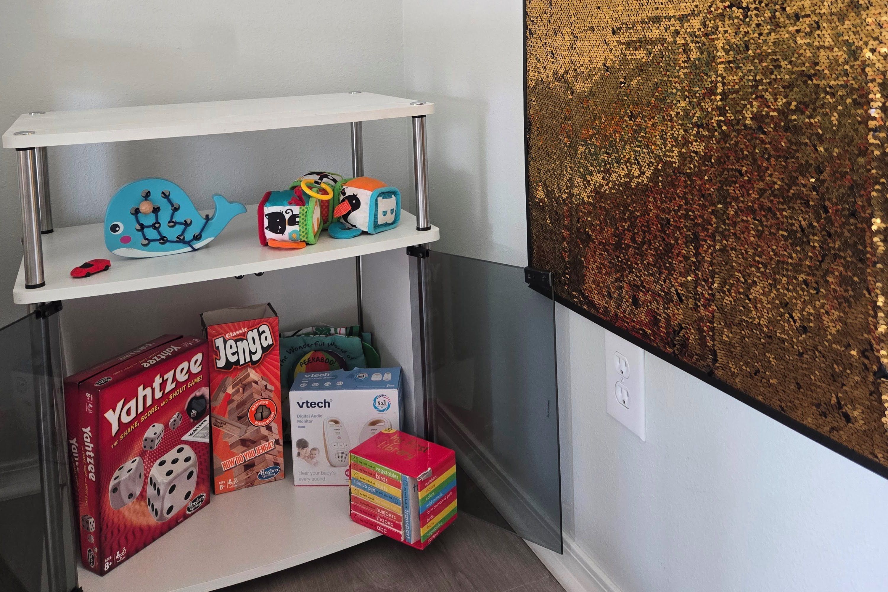 Une étagère avec des jouets et des jeux, un jeu de dés et un moniteur audio numérique.