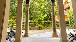 Ein architektonisches Bogenportal mit Säulen, eine Decke mit dekorativen Fresken und Blick auf Grünflächen sowie abgestellte Fahrräder.