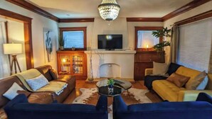 A cozy living room with a fireplace, a television mounted above it, and two sofas facing each other. - Craftsman 4 Bed/2 Ba. Home Sleeps 10, AC & Parking (Long Beach)