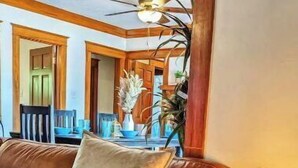 A brown leather sofa with a cushion, a round side table with a mosaic pattern, and a ceiling fan in a room with wooden beams and a visible kitchen area in the background. - Craftsman 4 Bed/2 Ba. Home Sleeps 10, AC & Parking (Long Beach)