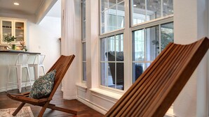 Une pièce comprenant un fauteuil à bascule en bois, un banc blanc avec coussin et une grande fenêtre donnant sur l’extérieur.