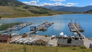 Un port de plaisance avec des bateaux amarrés, un petit bâtiment et une vue dégagée sur les collines et les montagnes environnantes.