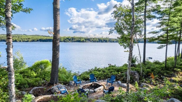 Blick auf einen See mit vier blauen Adirondack-Stühlen und einer felsigen Uferlinie.